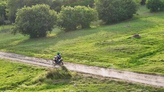 航拍一名摩托车越野赛车手在尘土飞扬的乡村公路上行驶在无人机的追逐下快速探索美丽的大自然