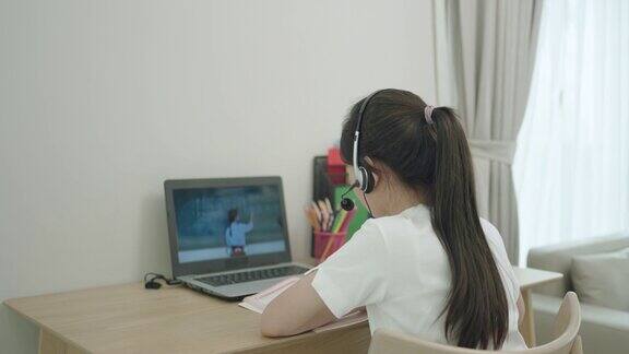 一名亚洲少女在学校因新冠肺炎疫情关闭期间在家中的客厅通过笔记本电脑与老师在线学习数学