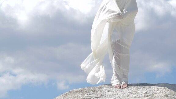 一个美丽的女人穿着飘动的白色衣服站在山顶上对着天空天使存在的幻影200帧秒的慢动作