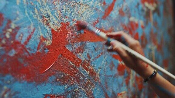 近距离拍摄的女性艺术家的手拿着画笔和绘画与红色油漆色彩缤纷情感丰富的油画创作现代抽象艺术作品的当代画家