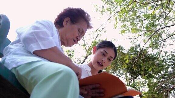 照顾老人的一个女孩(妇女)和祖母坐在一个平装本上读一本书在公园里概念公寓疗养院养老院帮助老人