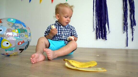 可爱的婴儿坐在地板上吃香蕉手里拿着香蕉的帅哥