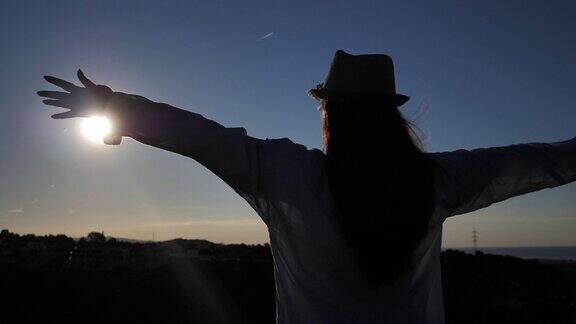 女孩站在山顶望着城市和大海黎明时分她的双手伸向太阳