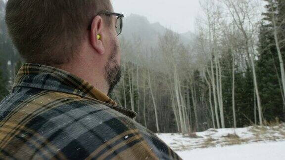 一个白种男人在他三十多岁的胡子把耳塞在他的耳朵在一个雪天在山上的树林里
