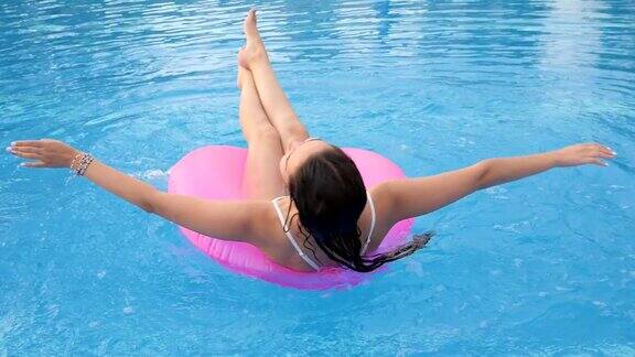 在夏天休息时漂亮的女孩穿上泳装在粉红色的充气环上旋转