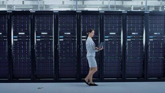 女性数据中心IT工程师带着笔记本电脑穿过服务器机架走廊她正在视觉检查工作服务器机柜