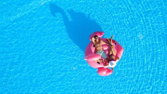 天线:穿着泳衣的男人和女人躺在有趣的粉红色充气火烈鸟浮上