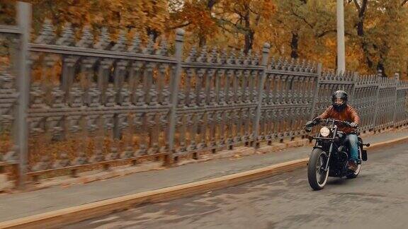 骑摩托车的人戴着头盔穿过城市的街道秋天的旅行侧视图