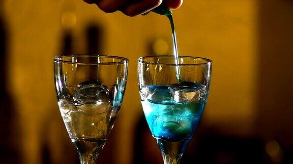 酒吧里的调酒师在调制鸡尾酒用两杯冰加蓝色液体还有同志酒吧近距离慢镜头