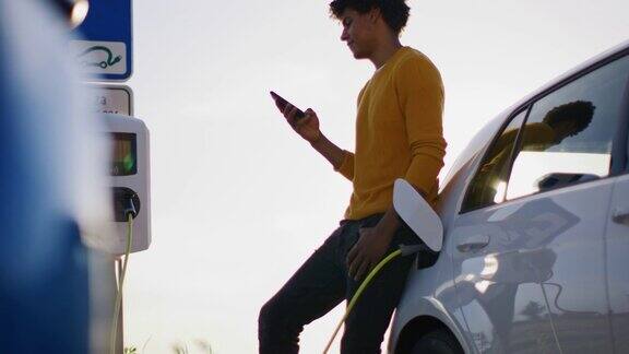 一名年轻男子在给电动汽车充电时使用智能手机
