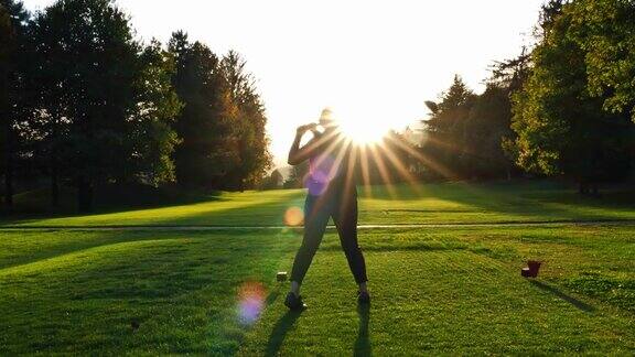 在一个阳光明媚的秋天高尔夫球手和她的司机在阳光和镜头光晕下的高尔夫球场上开球