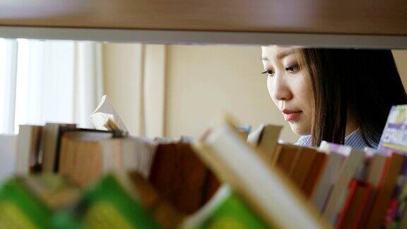 美丽的亚洲认真的女学生站在书架附近的书籍在大图书馆拿着教科书翻页阅读