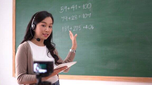 微笑的亚洲女教师在耳机工作在课堂教学在线解释黑板上的数学学生从家里学习的肖像远程教育隔离期间COVID-19疫情