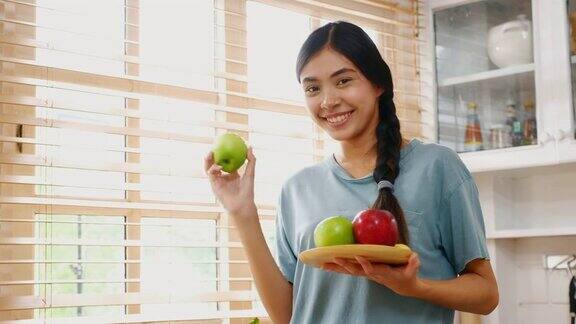 年轻的亚洲女人拿着苹果与幸福在家里的厨房人们健康的生活方式