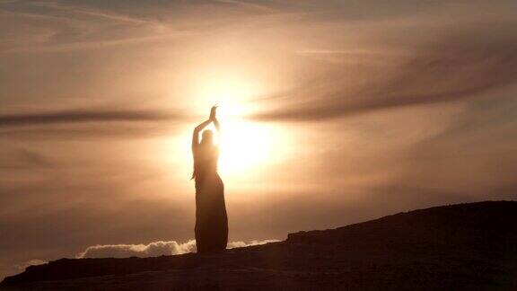 日落时分一个女子在沙丘上跳东方肚皮舞的剪影