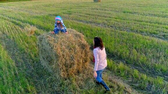 小女孩坐在草堆上把稻草扔给妈妈