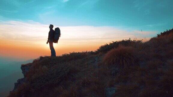 一个背着旅游背包的人走在一座日落背景的山上