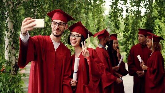 一对欢快的应届毕业生正在用智能手机自拍一男一女拿着文凭微笑着看着智能手机的摄像头