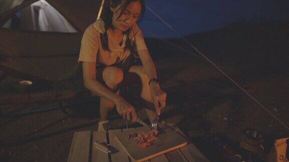 在泰国清迈夜色中年轻女子在篝火露营时做牛排