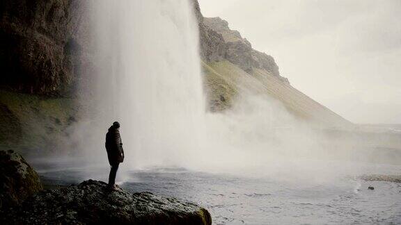 一名年轻男子带着摄像机站在冰岛的Gljufrabui瀑布附近拍摄水流的视频