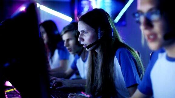 在一场网络游戏锦标赛上玩竞技电子游戏的职业电竞玩家团队女孩和男孩戴上耳机舞台被霓虹灯照亮