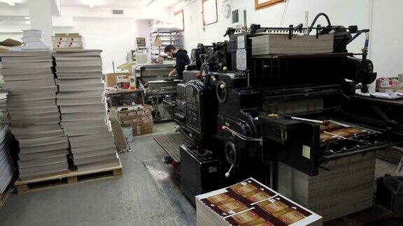当工人在后台工作时机器在印刷厂分类堆叠的印刷媒体