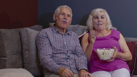 一对老夫妇抱着爆米花坐在客厅的沙发上看恐怖电影