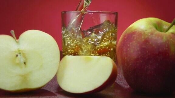 在红色背景的慢镜头中将新鲜的苹果汁倒入玻璃杯中