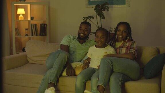 快乐的年轻家庭聚在一起在电视前看电影在晚上