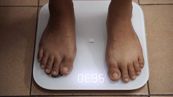 一个女人在电子秤上检查他的体重