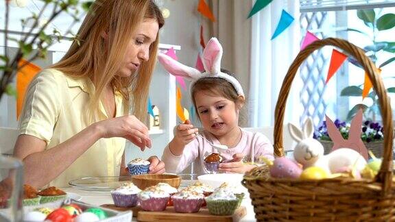 年轻的母亲和她的女儿戴着兔子耳朵做复活节纸杯蛋糕