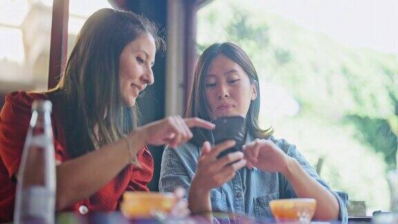 两个多民族的女性朋友在咖啡馆里一起玩手机