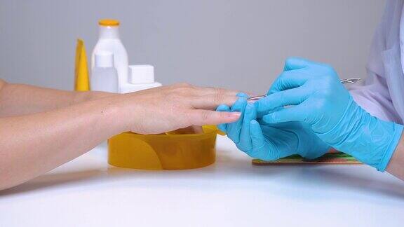 在水疗沙龙中客户的手和美甲师在处理手套上的指甲时会在去除指甲之前竖起一个角质层指甲护理