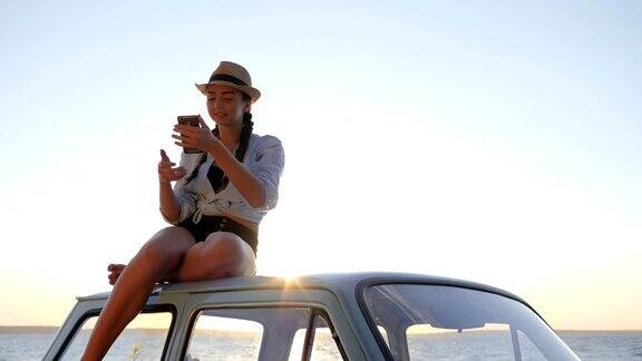 女孩对着海边的老爷车车顶自拍女人对着老机器用手机拍照
