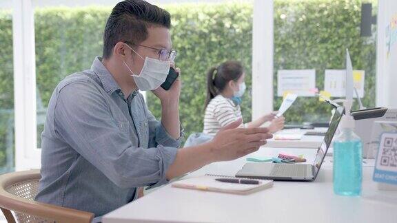 亚洲工人戴着口罩在办公室用笔记本电脑工作社交距离衡量冠状病毒危机后的生活方式商务人士一起在办公室工作的新常态