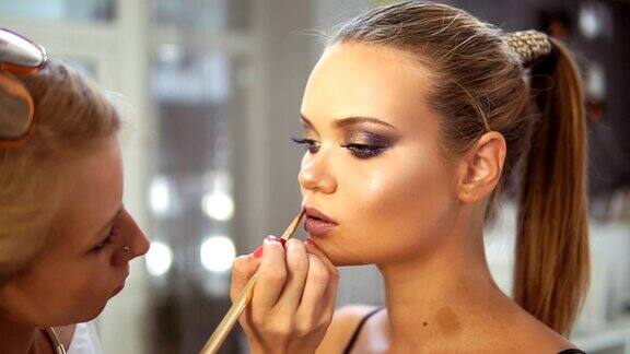 不可辨认的专业化妆师用特殊的画笔在模特的嘴唇上涂抹口红在嘴唇上涂唇彩专业化妆