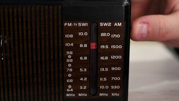 在一张旧木桌上收音机里播放着无线电波拧一下旧的听筒怀旧的生活方式把模拟收音机调到一个音阶上一个男人在用一台旧收音机听新闻