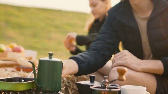 美丽的年轻白种人夫妇享受野餐在日出靠近的咖啡壶咖啡杯茶杯煎蛋锅炉子上野餐
