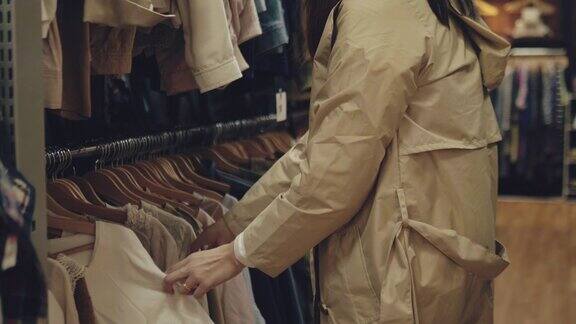 年轻的亚洲女人在购物中心的货架上挑选衣服