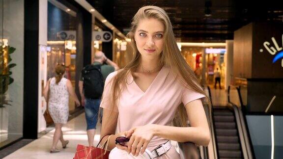 年轻迷人的女孩站在商场里拎着包看着镜头购物概念时尚概念