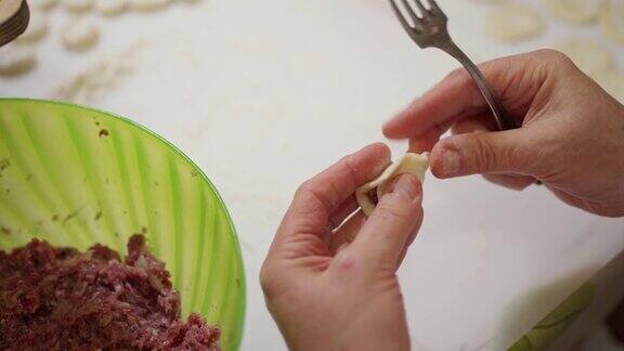 女性手用叉子从大碗里挑肉末然后把饺子馅放进面团里