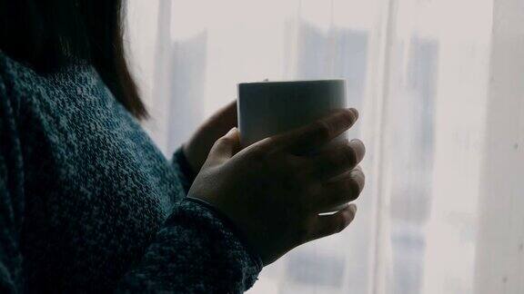 一个女人拿着咖啡靠近窗户的特写