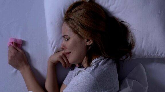 哭泣的女士躺在床上抱着粉红色的婴儿袜子产后抑郁