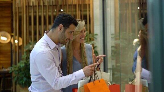 一对美丽的拉丁美洲夫妇在购物中心看着商店的橱窗一边说一边指着