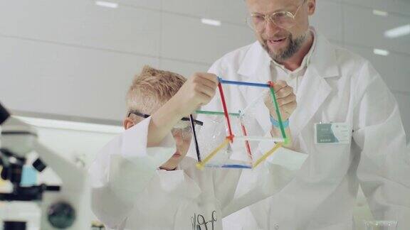 男孩和他的老师一起做科学实验在实验室里玩得很开心用肥皂泡液研究表面张力