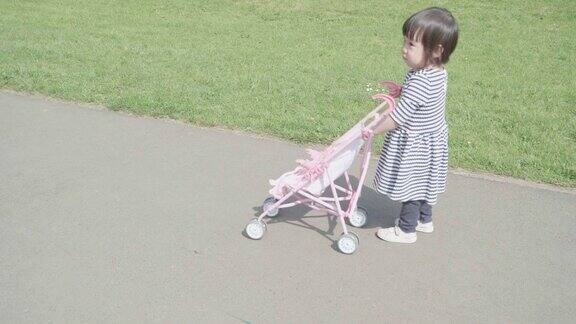 初学走路的小女孩在春天的花园里拖着玩具婴儿车