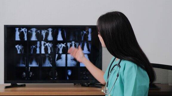 在医院里一位亚洲女医生正对着摄像机解释监视器上的x光胶片信息