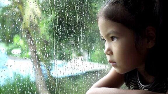 亚洲小女孩看着窗外的雨慢镜头