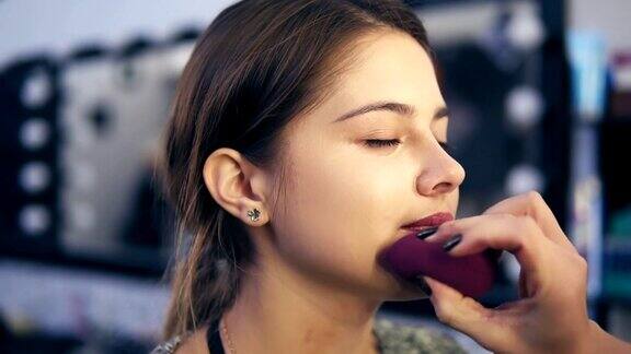面相师用海绵在年轻女子脸上涂抹粉底液美容院专业化妆Slowmotion拍摄