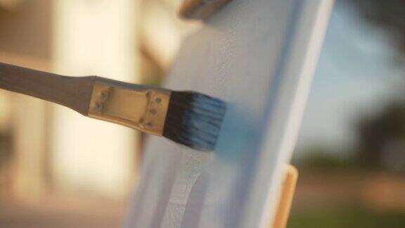 在户外阳光下特写画笔在画布上作画一个陌生的年轻白人女画家在夏日早晨的阳光下在画架上作画缓慢的运动